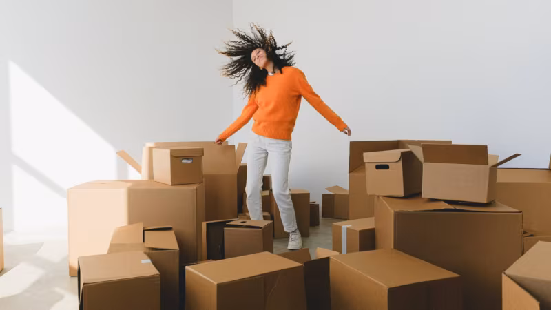 A woman standing among many cardboard boxes with her hair flying