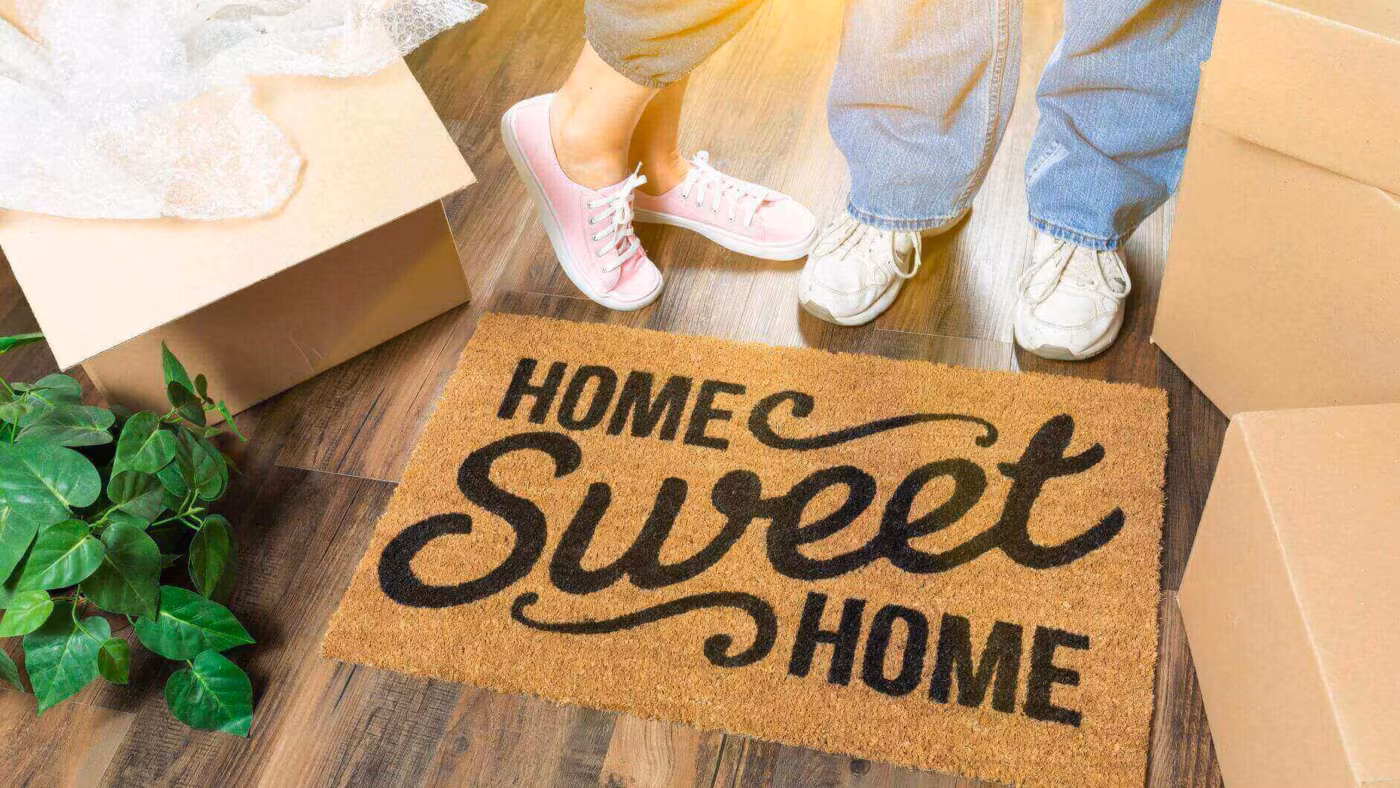 two people unpacking in front of a mat saying 'home sweet home' after long-distance moving
