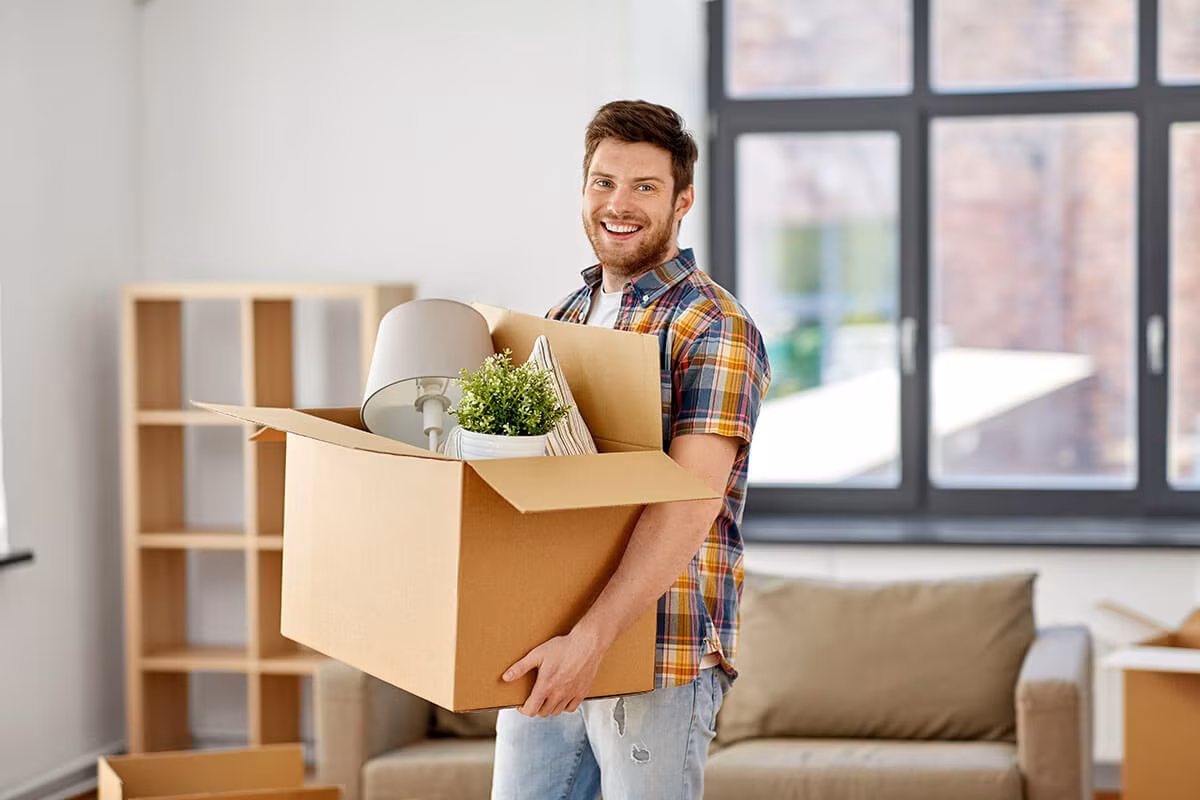 A man carrying an open box of belongings through a bright room