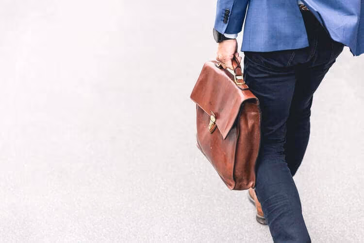 A person walking away carrying a leather satchel