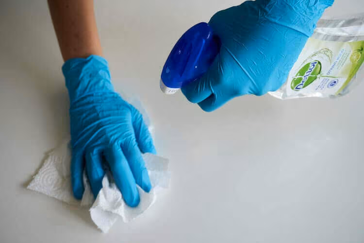 Gloved hands wiping a surface with a cloth and a cleaning spray