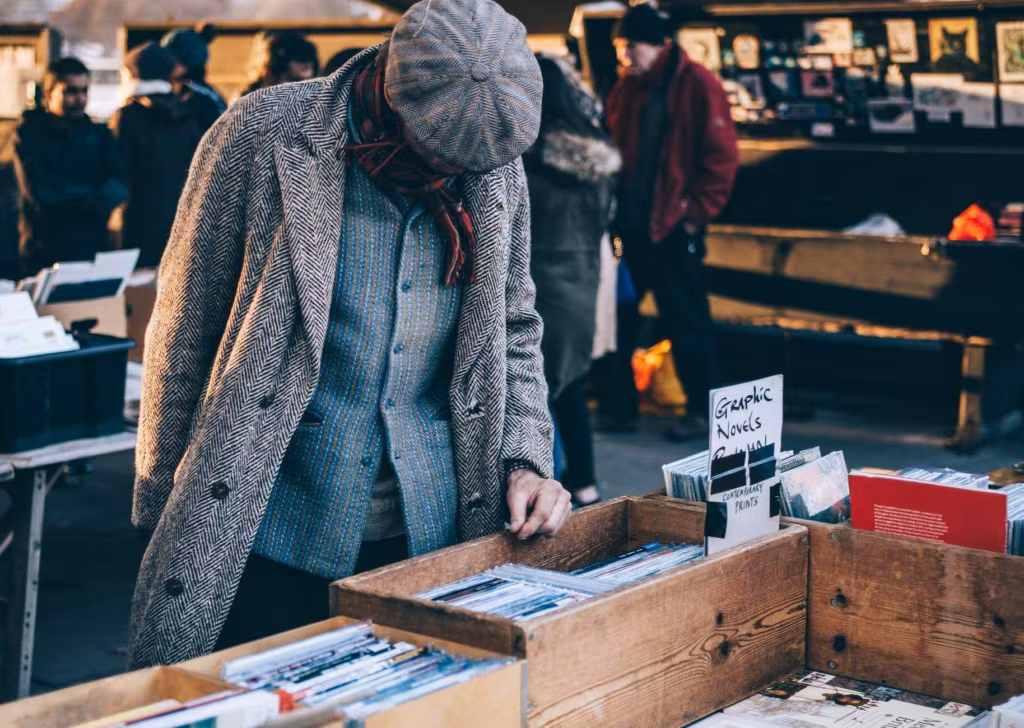 A person in a coat and hat browsing a crate of records at an outdoor market