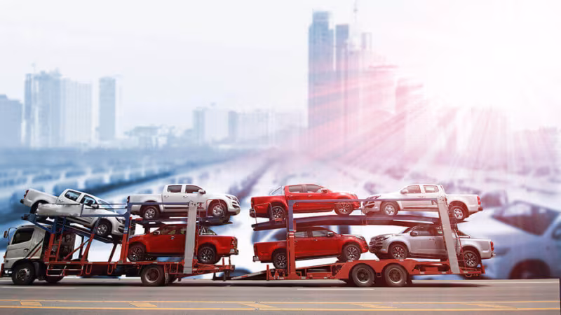 A car transporter loaded with cars on a road with a city skyline behind