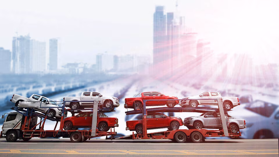 A car transporter loaded with cars on a road with a city skyline behind