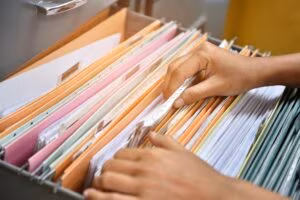 Hands searching through colored hanging files in an open filing drawer