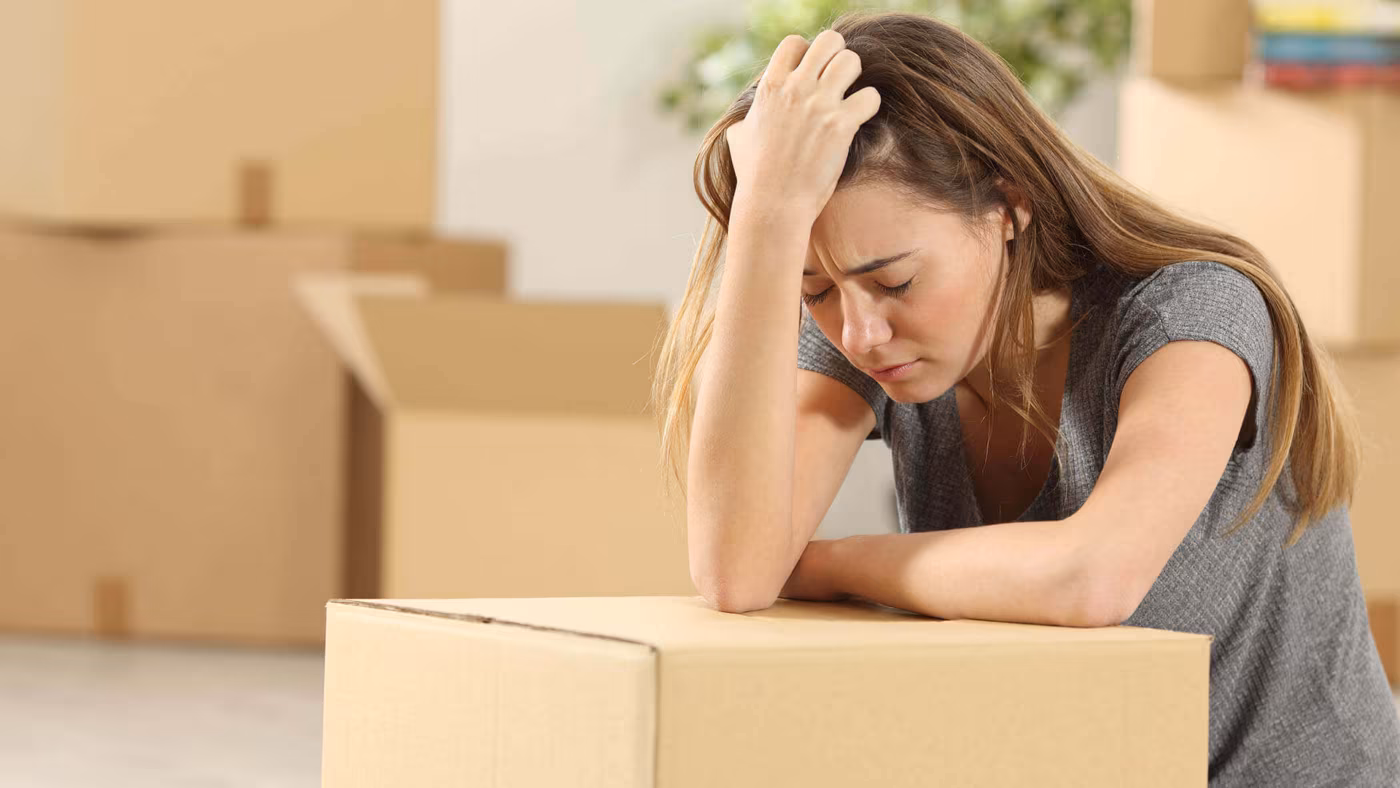 A woman leaning on a cardboard box with a hand to her head