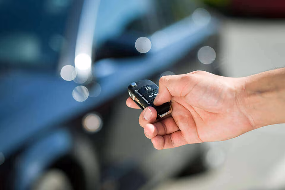 A hand holding a car key fob beside a car door
