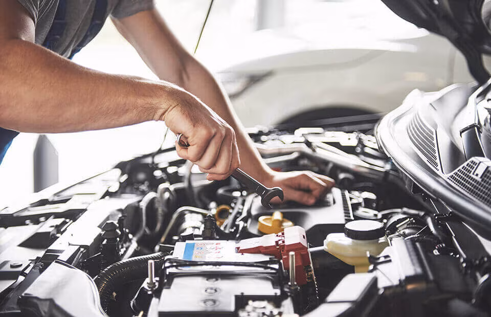 Hands working on a car engine under an open bonnet