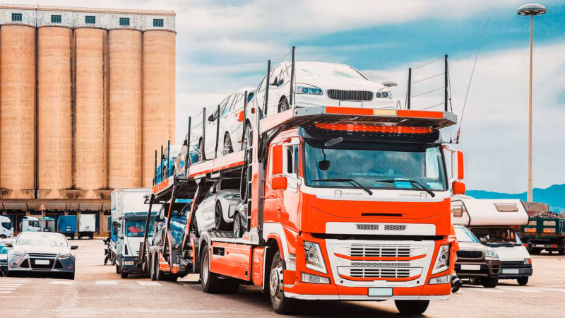 A red car transporter lorry loaded with cars at a depot