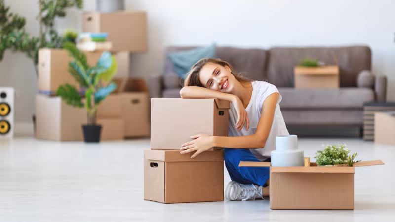 A woman resting her head on a cardboard box on the floor of a part-packed room