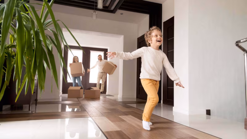 A child running through a bright hallway while adults carry boxes in behind