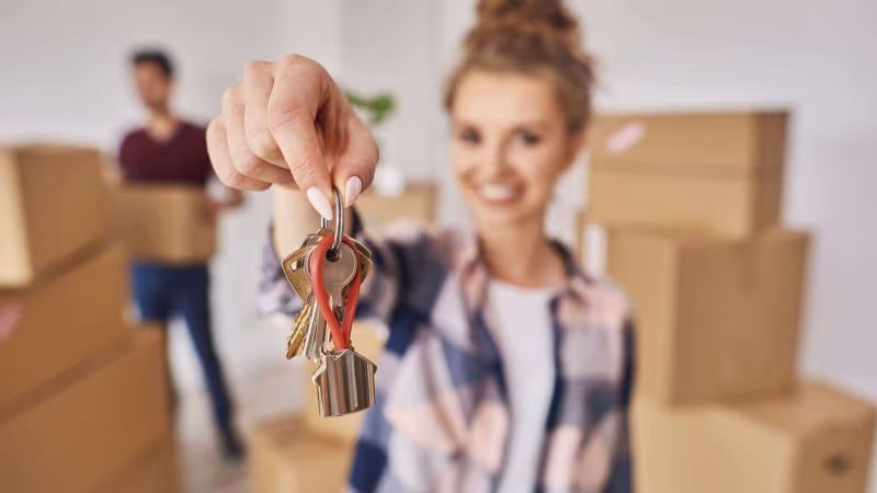 A woman holding up a set of keys among cardboard boxes
