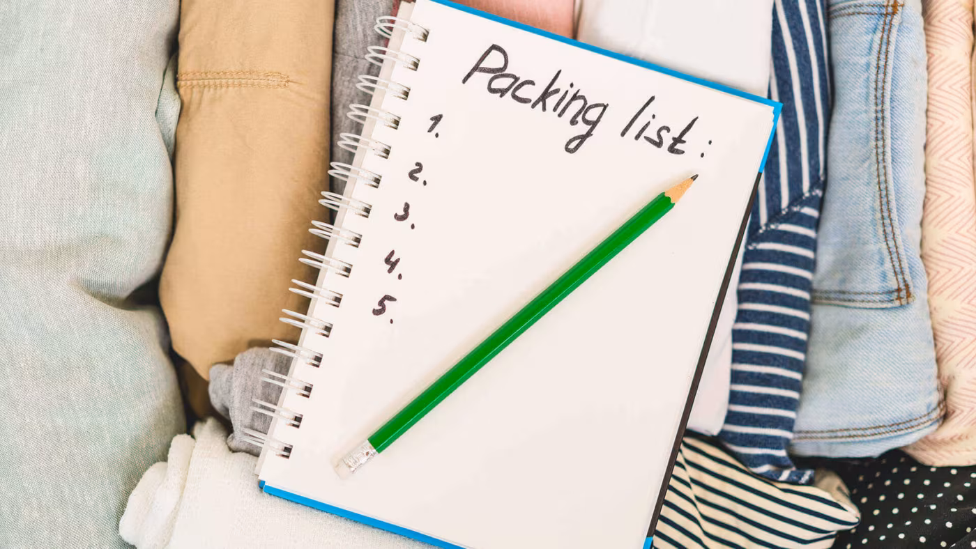 A notebook headed Packing list with numbered lines, resting on folded clothes