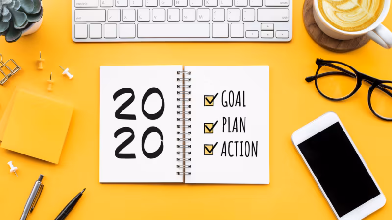 Seen from above, a notebook headed 2020 with goal, plan and action ticked, beside a keyboard and a phone