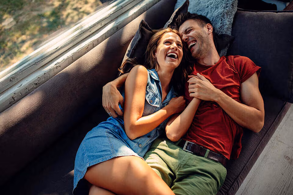 A couple lying together on a sofa, laughing