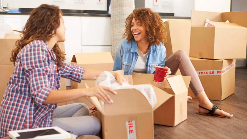 Two women sitting on the floor unpacking a box marked Fragile