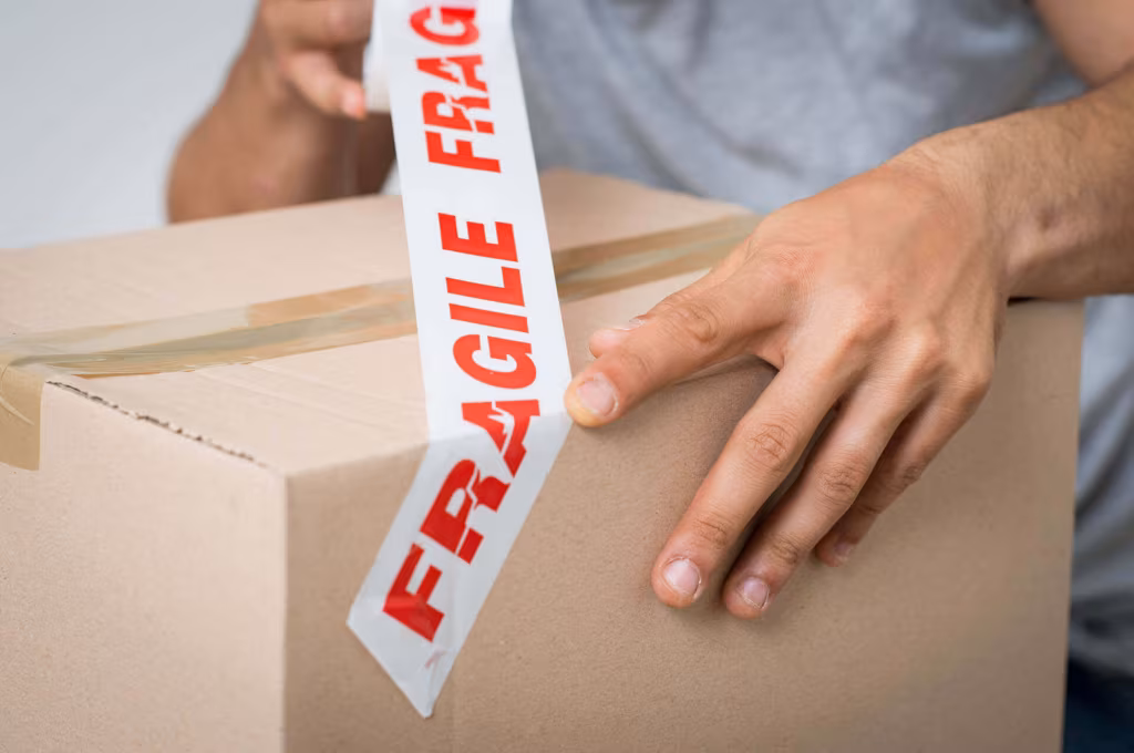 Hands applying red Fragile tape to a cardboard box