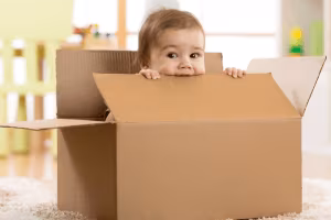 A baby peeking over the edge of a large cardboard box