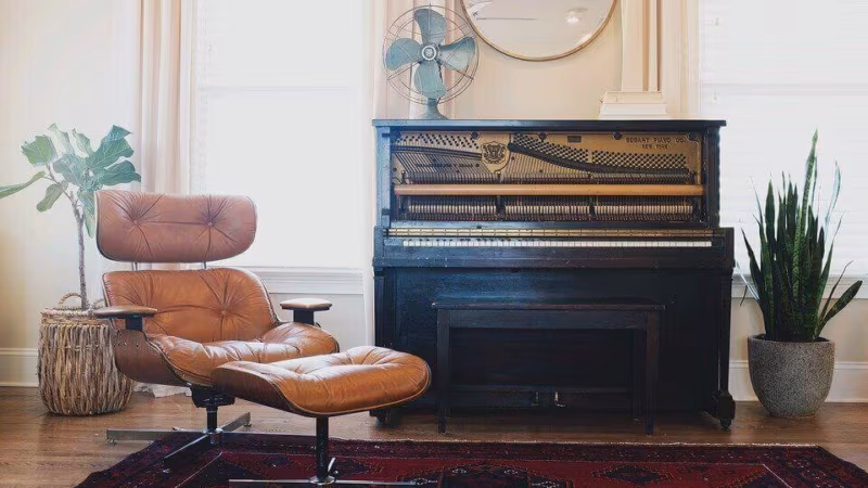 An upright piano and a leather lounge chair in a bright room with a patterned rug