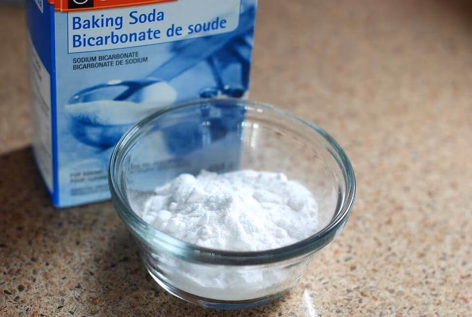A box of baking soda beside a glass bowl of the powder