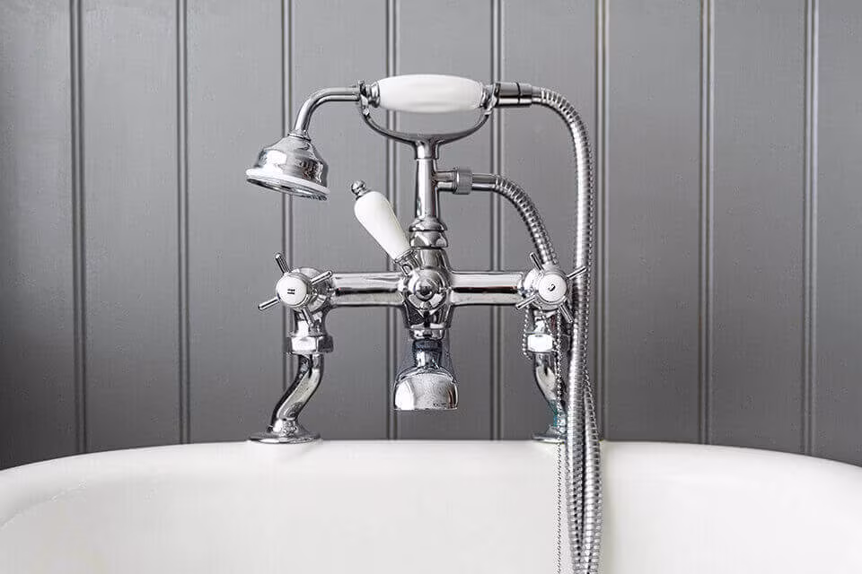 A chrome bath tap and hand shower over a white bathtub against grey wall panelling