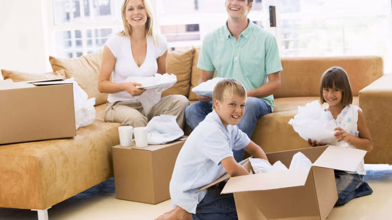 A family sitting on and beside a sofa unpacking a box of crockery
