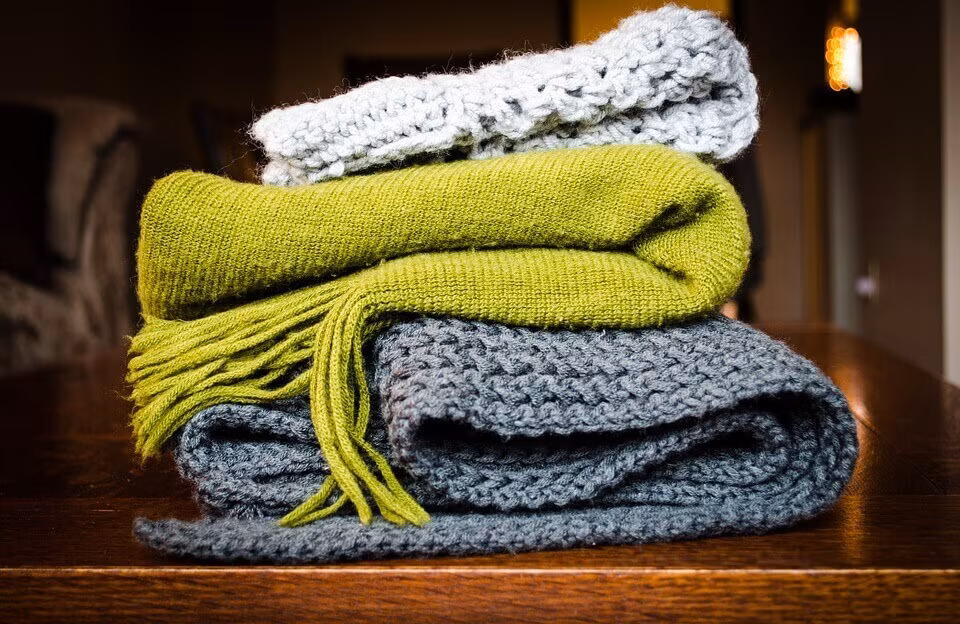 Folded blankets in green, grey and cream stacked on a table