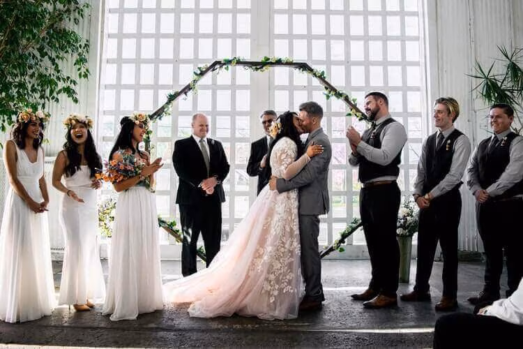 A bride and groom embracing under a floral arch with their wedding party on either side