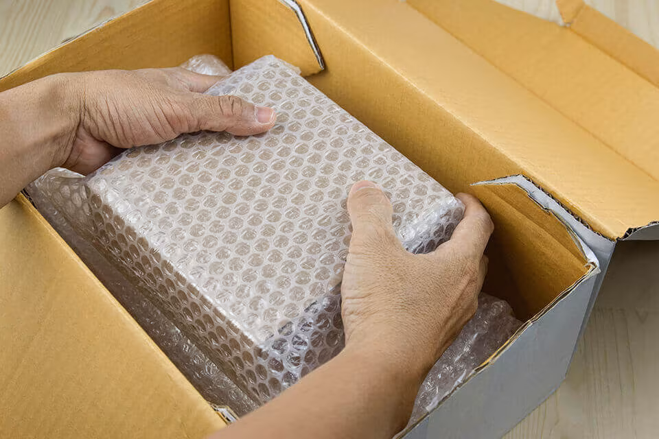 Hands lowering a bubble-wrapped parcel into a cardboard box