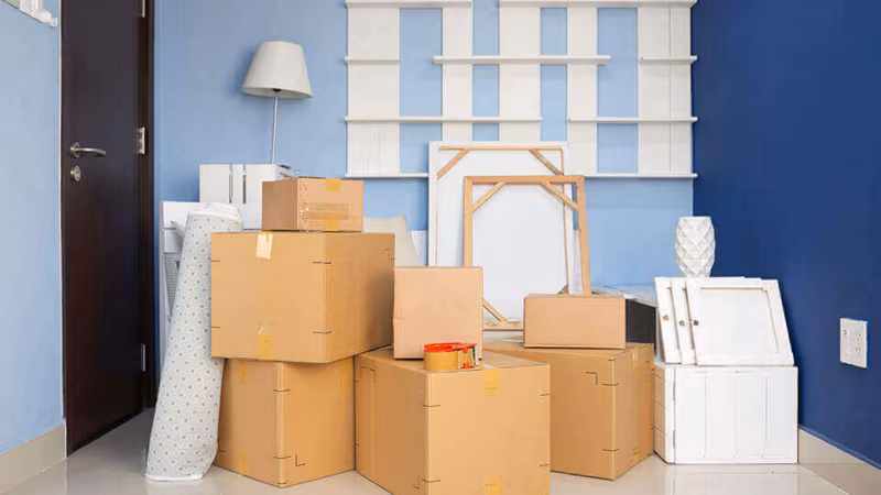 Cardboard boxes stacked in an empty room against a blue wall