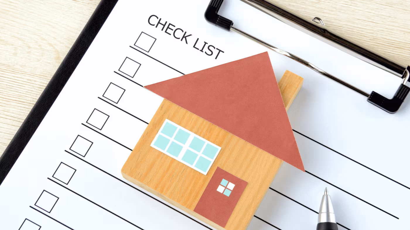 A paper cut-out house on a clipboard checklist with empty tick boxes and a pen