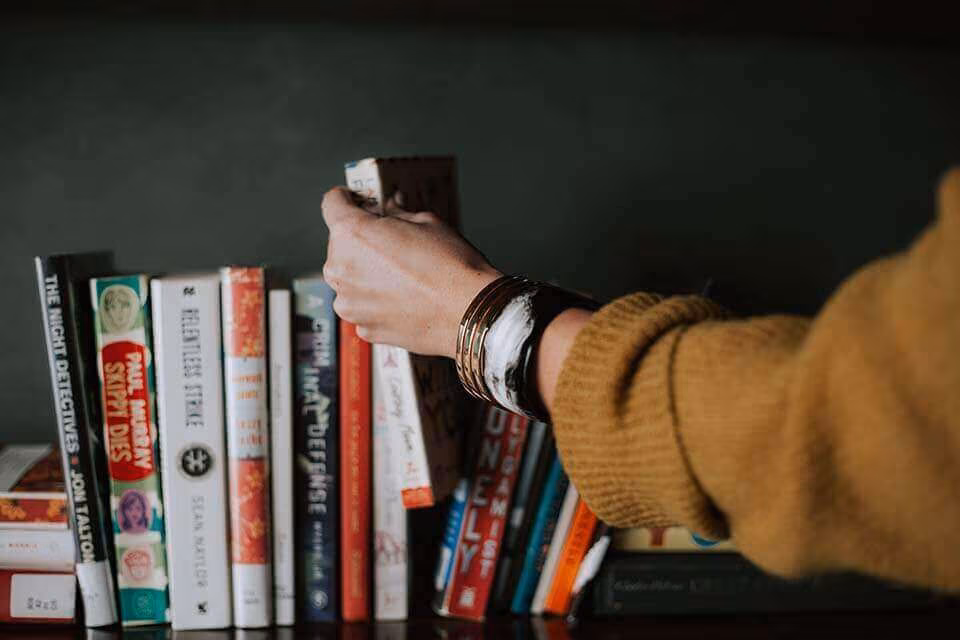 A hand pulling a book from a crowded bookshelf