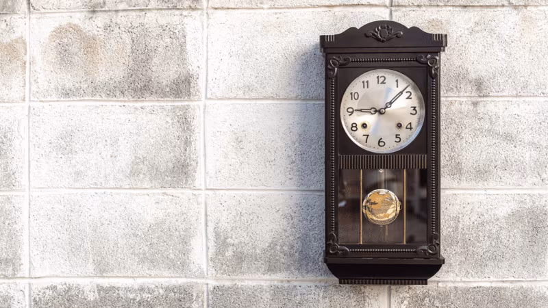 A dark wooden pendulum wall clock on a white brick wall