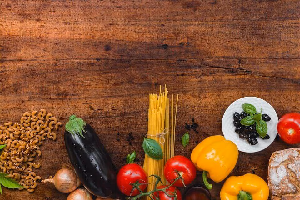 Vegetables, pasta, olives and bread arranged on a dark wooden table