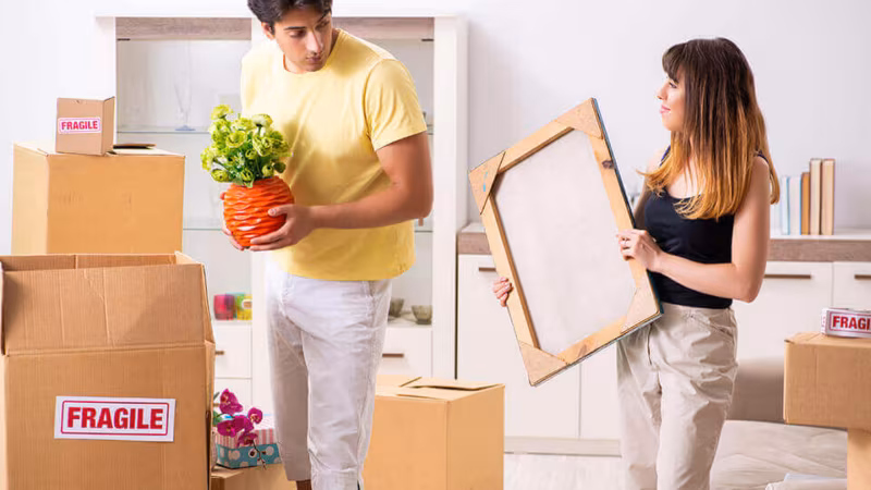 A couple unpacking a plant and a picture frame among boxes marked Fragile