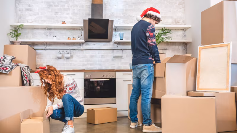 A couple in Christmas hats packing cardboard boxes in a kitchen