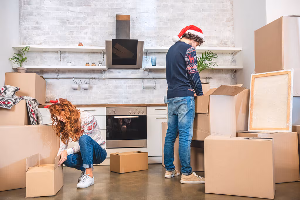 A couple in Christmas hats packing cardboard boxes in a kitchen