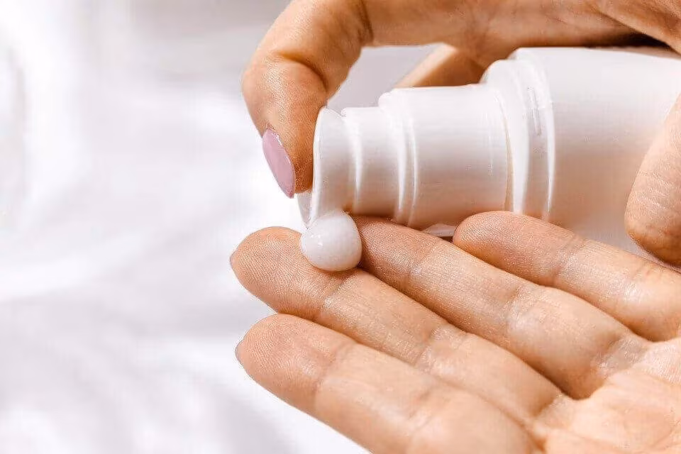 A hand squeezing lotion from a white bottle into the other palm