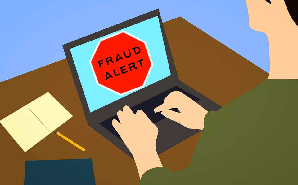 An illustration of hands at a laptop displaying a red fraud alert sign
