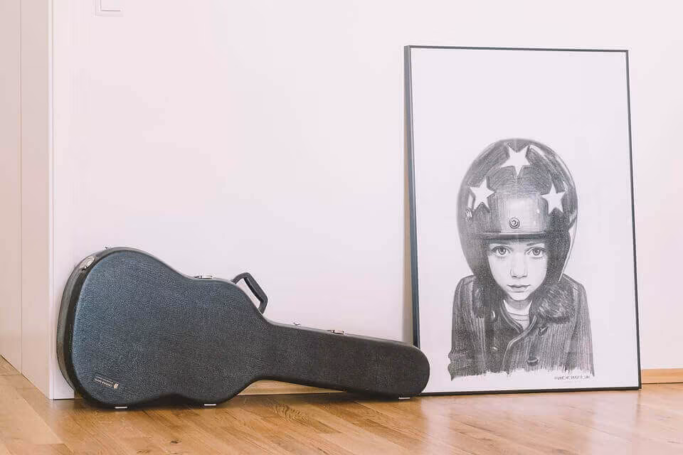 A guitar hard case standing on a wooden floor beside a large framed print