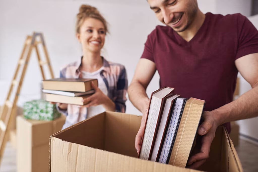 A couple packing books into a cardboard box
