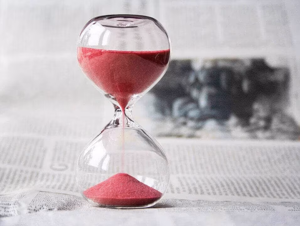 An hourglass with red sand standing on a newspaper