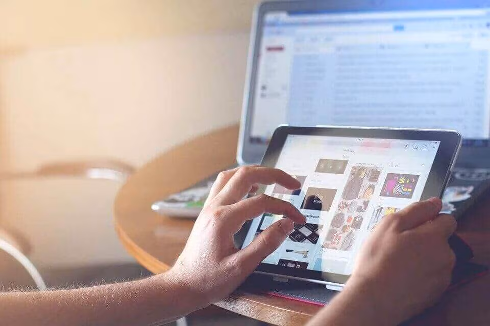 Hands using a tablet beside a laptop on a desk