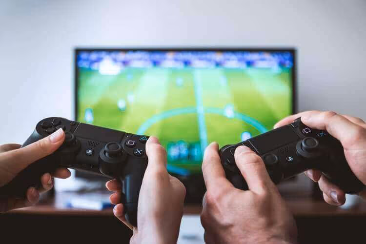 Two people holding game controllers in front of a television showing a football match