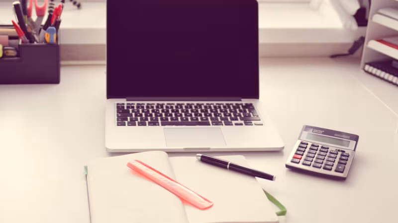 A laptop, a notebook, a pen and a calculator on a desk