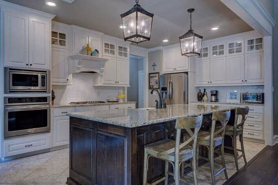 A large white kitchen with a dark island, pendant lights and bar stools