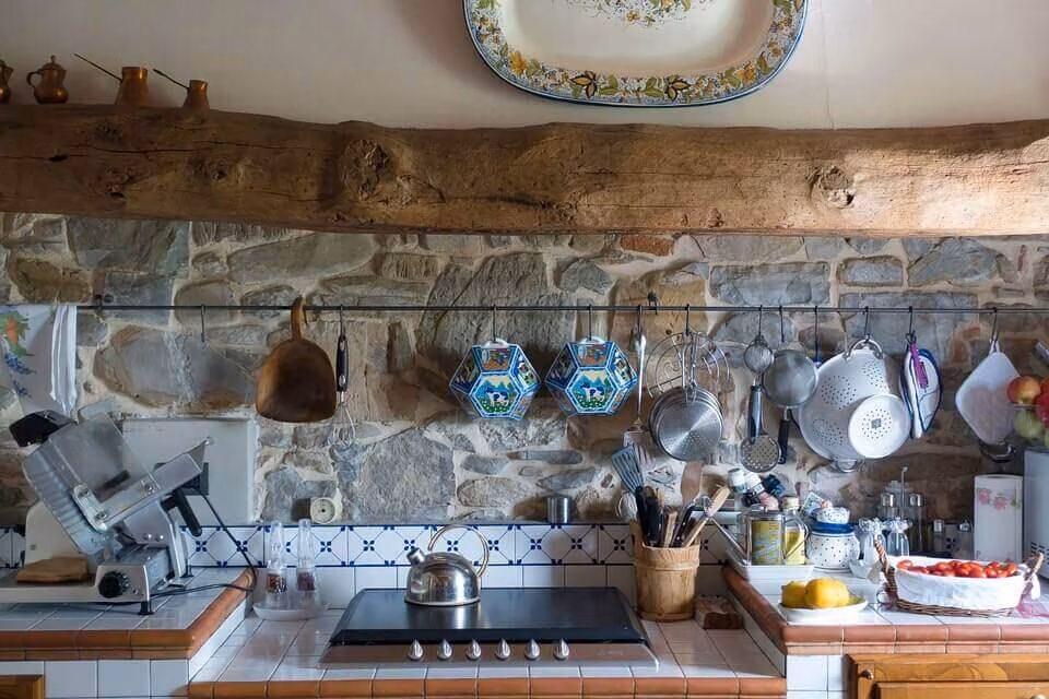 A rustic kitchen with a stone wall and pans hanging from a wooden beam