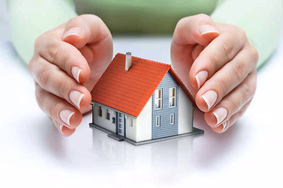 Two hands cupped protectively around a model house