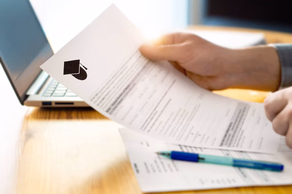 Hands holding a printed form beside a laptop and pens on a desk