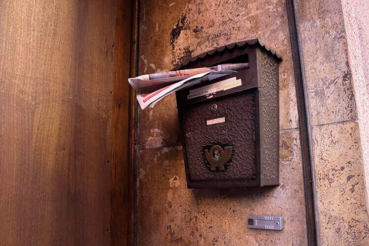 An old metal letterbox on a weathered wall stuffed with post